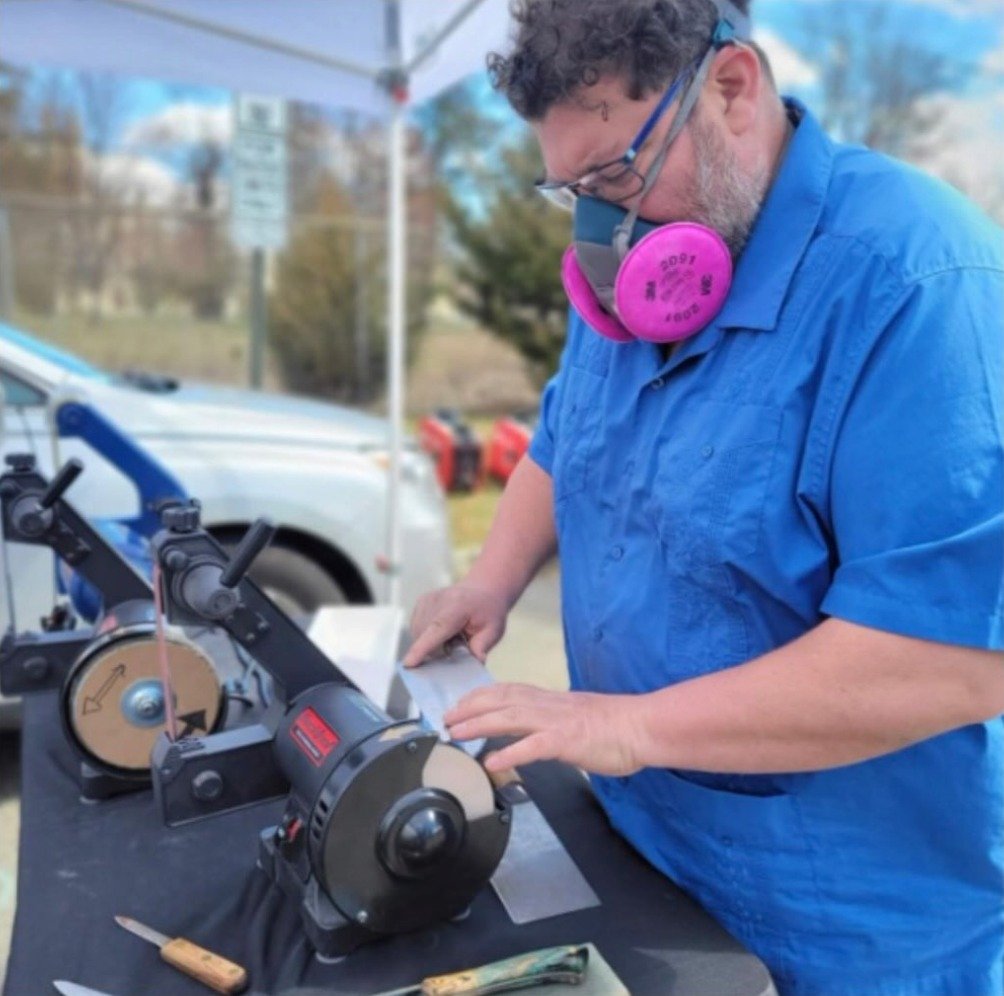 Roberto of Hudson Grinding sharpening a knife on a slow-speed grinder at the Nyack Farmers Market